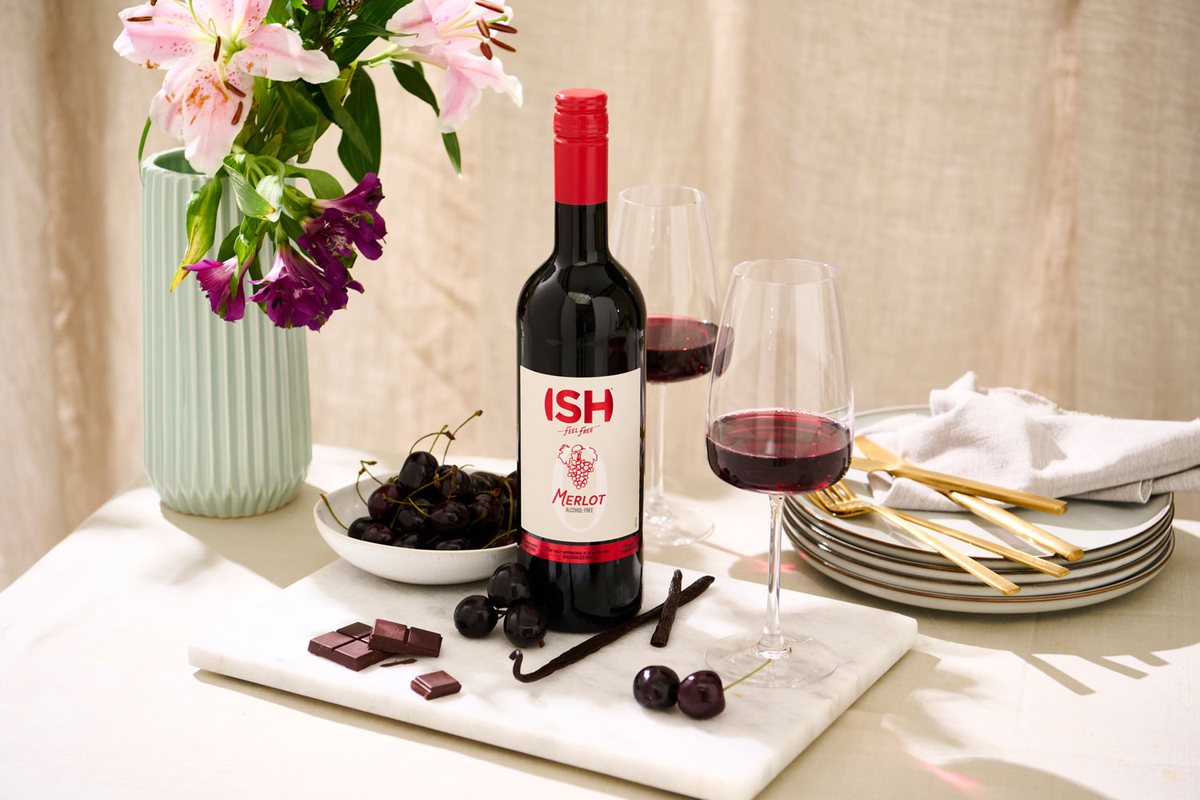 Flasche alkoholfreier Merlot mit zwei Gläsern, Blumen und Schokolade