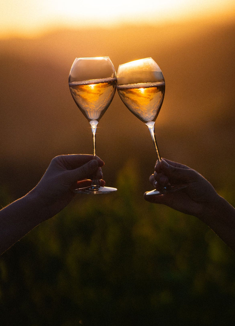 Zwei Gläser mit alkoholfreiem Sparkling stoßen im Abendlicht über den Weinbergen an.