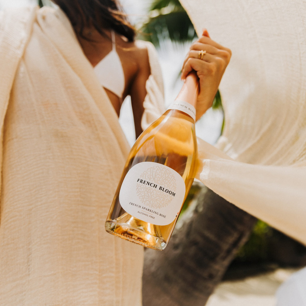 French Bloom Le Rosé in der Hand, helles Tuch im Wind, Palmen