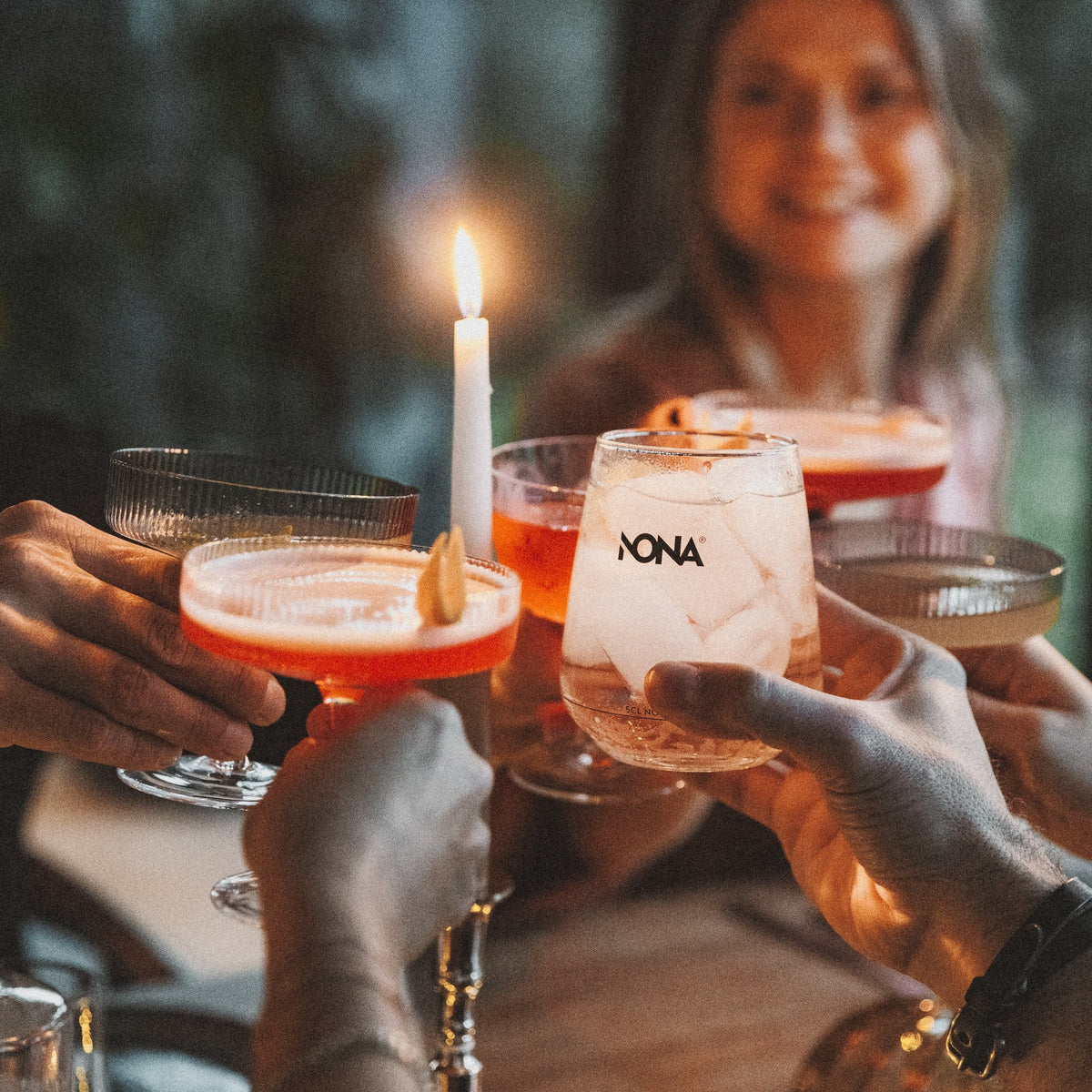 Freunde stoßen bei Kerzenlicht mit NONA Spritz-Drinks an
