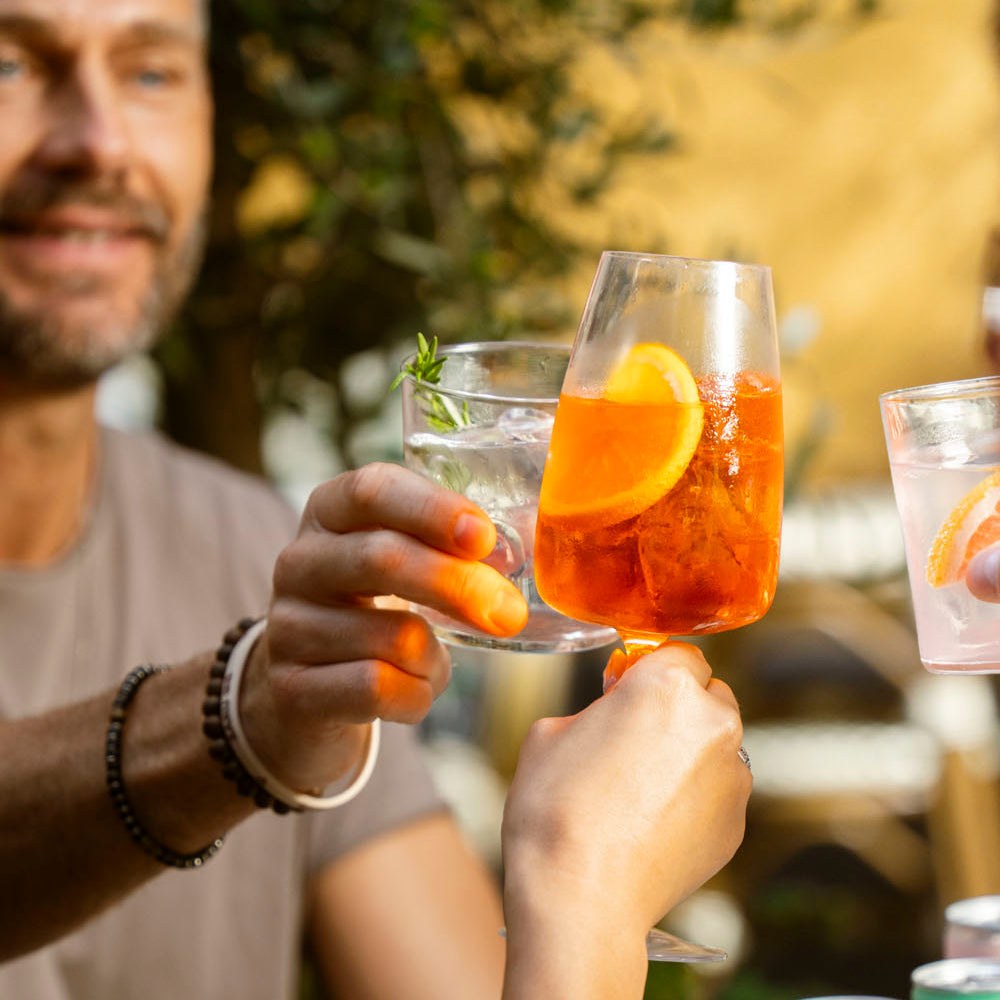 Freunde stoßen im Freien mit Spritz und Mojito im Glas an