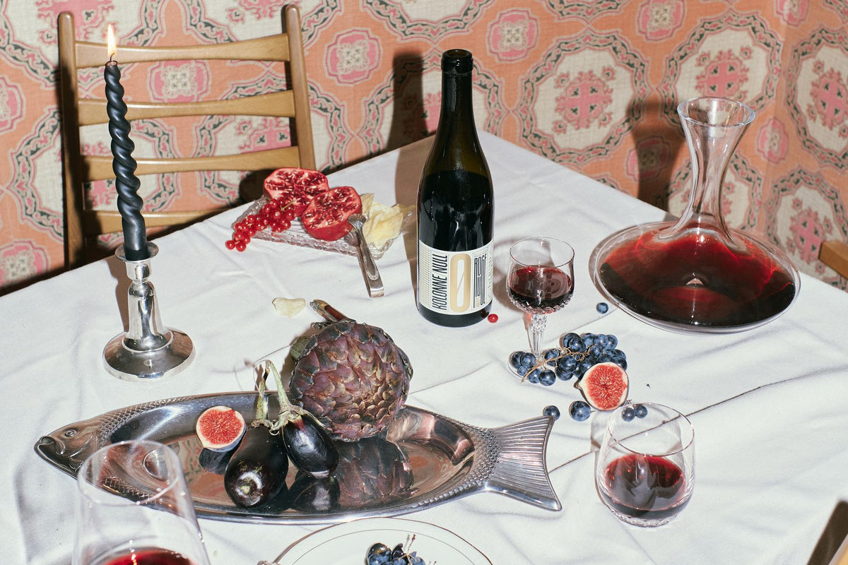 Festlich gedeckter Tisch mit Kerze, Karaffe und alkoholfreiem Rotwein