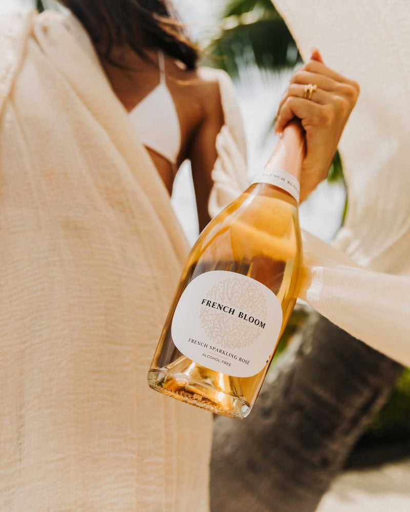 Eine Flasche French Bloom Le Rosé in der Hand, vor hellem Leinen in der Sonne.